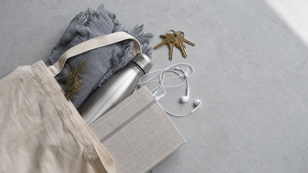 An overhead view of a tote bag with everyday essentials — keys, notebook, water bottle, headphones — for a portable wind-down routine that fits a busy life.
