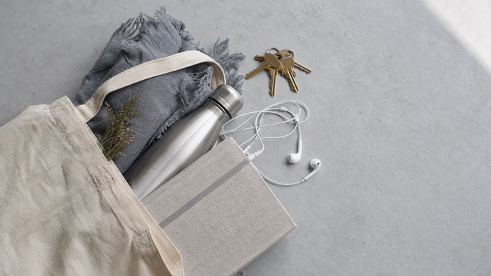 An overhead view of a tote bag with everyday essentials — keys, notebook, water bottle, headphones — for a portable wind-down routine that fits a busy life.